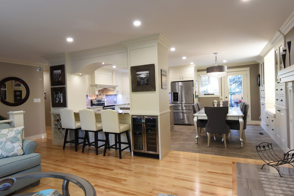 Inspiration for a mid-sized transitional u-shaped light wood floor and gray floor open concept kitchen remodel in Calgary with an undermount sink, beaded inset cabinets, white cabinets, granite countertops, gray backsplash, ceramic backsplash, stainless steel appliances, two islands and gray countertops