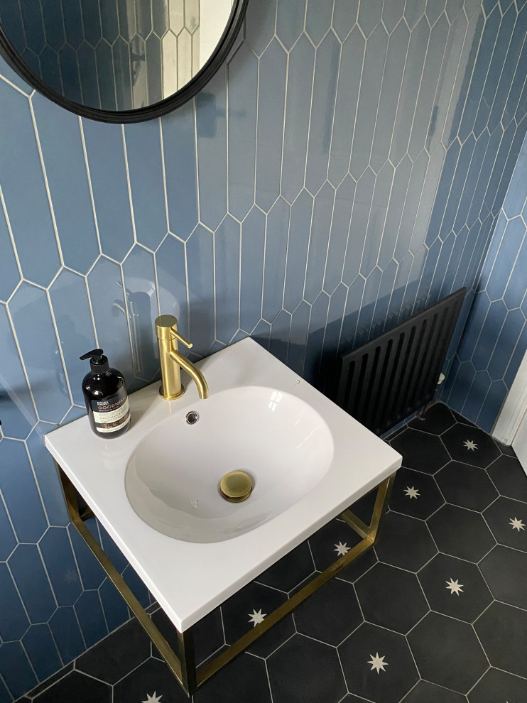 Photo of a small contemporary powder room in Other with a one-piece toilet, blue tile, ceramic tile, blue walls, cement tiles, a wall-mount sink, black floor and a floating vanity.