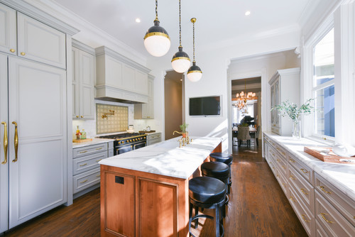 Elegant galley kitchen with soft-gray RTA cabinets, brass hardware, paneled refrigerator, long marble-topped wood island, and globe pendant lights.