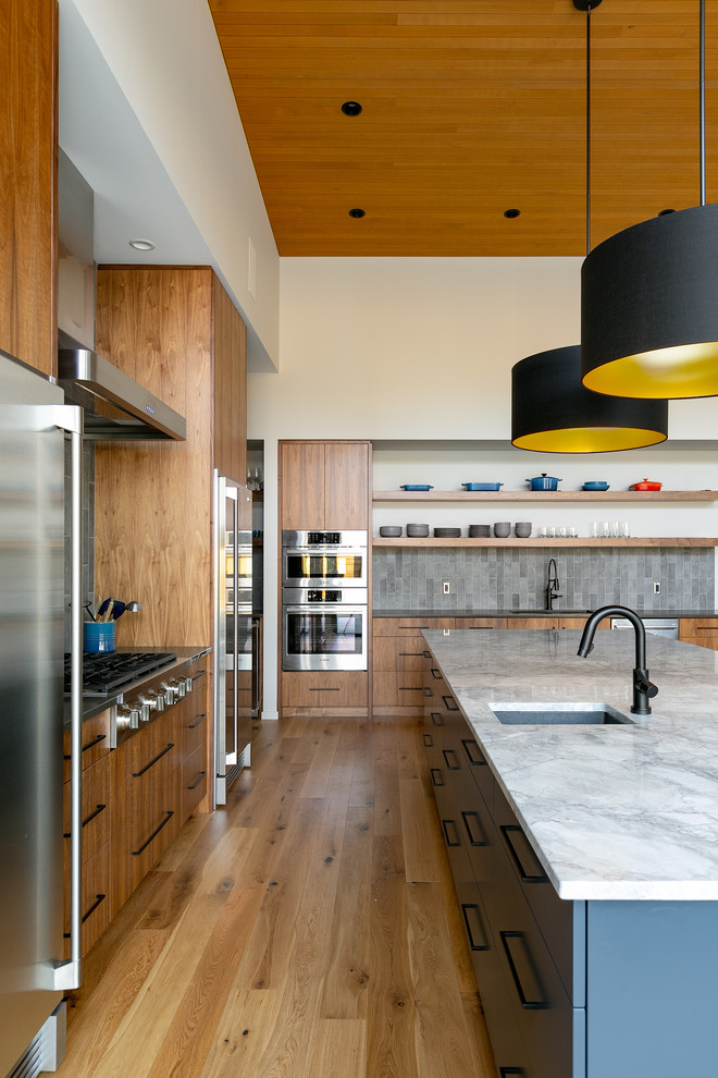 Inspiration for a large contemporary l-shaped open plan kitchen in Vancouver with an undermount sink, flat-panel cabinets, medium wood cabinets, marble benchtops, grey splashback, ceramic splashback, stainless steel appliances, light hardwood floors, with island, brown floor and grey benchtop.
