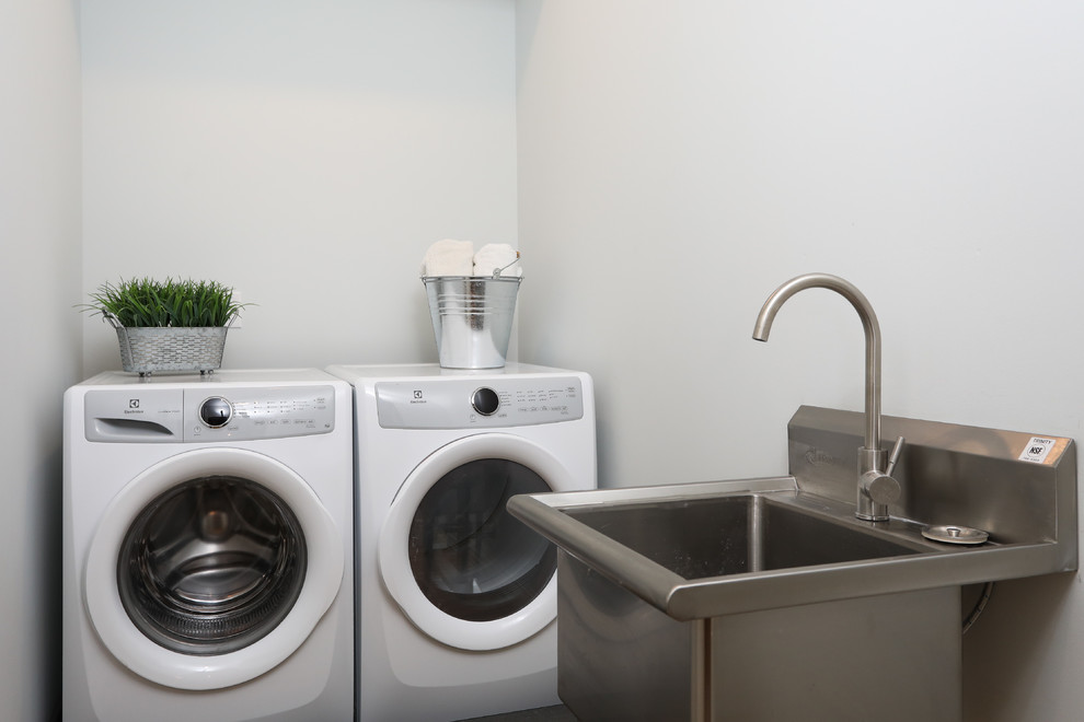 Example of a mid-sized transitional single-wall white tile gray floor and medium tone wood floor dedicated laundry room design with shaker cabinets, white cabinets, a one-piece toilet, gray walls, an undermount sink, gray countertops, an utility sink and a side-by-side washer/dryer