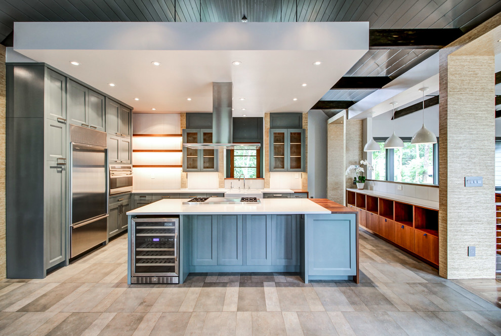 This is an example of a large contemporary u-shaped eat-in kitchen in Other with a farmhouse sink, shaker cabinets, blue cabinets, solid surface benchtops, white splashback, glass sheet splashback, stainless steel appliances, porcelain floors, with island and grey floor.