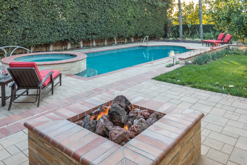 Design ideas for a mid-sized traditional backyard custom-shaped pool in Orange County with a hot tub and brick pavers.