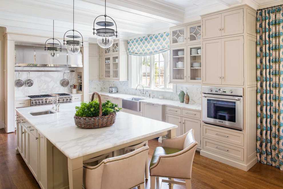 This is an example of a traditional l-shaped kitchen in DC Metro with a farmhouse sink, recessed-panel cabinets, beige cabinets, marble benchtops, white splashback, stainless steel appliances, medium hardwood floors and with island.