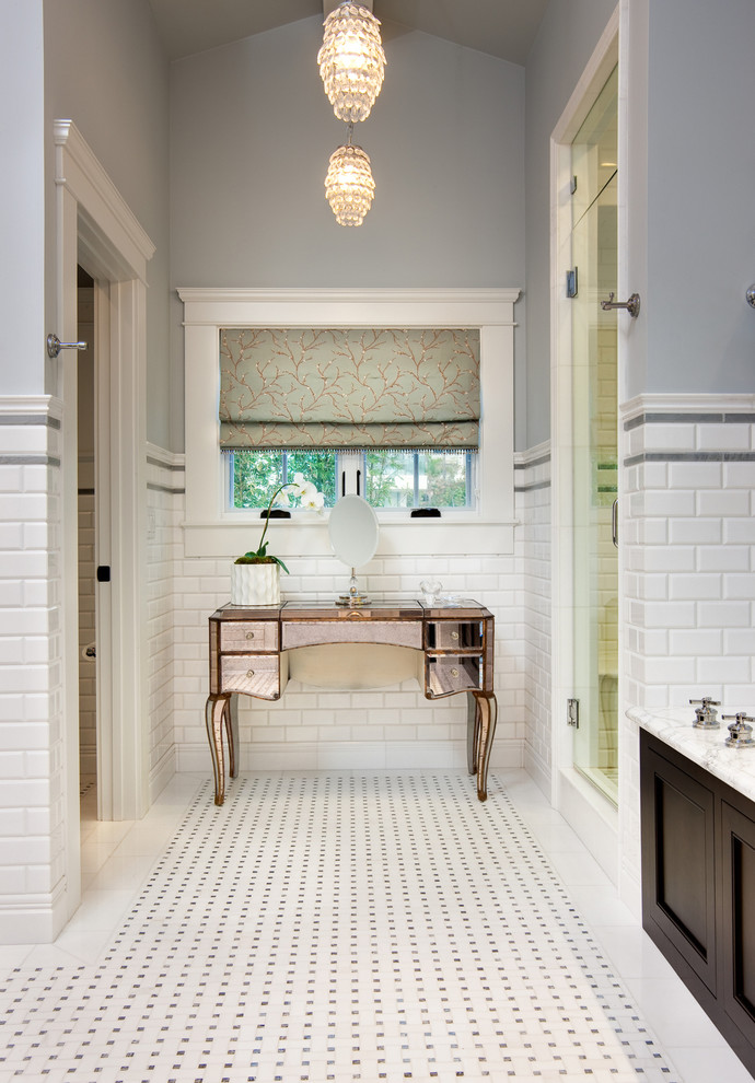 West Coast Hamptons - This Master Bathroom was created with light, ambiance and functionality in mind.  
The basketweave marble tile flooring is a classic tile bordered in a white thassos rectangular tile. The Thassos Beveled Brick is used for the tall wainscoting and shower walls with two rows of a thin grey tile accent.  The dark wood tone of the cabinet and face of the tub create a rich offset to the carrara marble countertop and tub top.  The vaulted ceiling helps to create the light open feeling.  The Horchow Mirrored Vanity is the focal point of the bathroom as it it perfectly centered underneath the window, boxed ridge beam, three crystal pendants and double door opening into the bathroom.  The sink cabinet was designed to look like a furniture piece with the custom feet at the toekick, pop out of the middle area and crystal hardware.