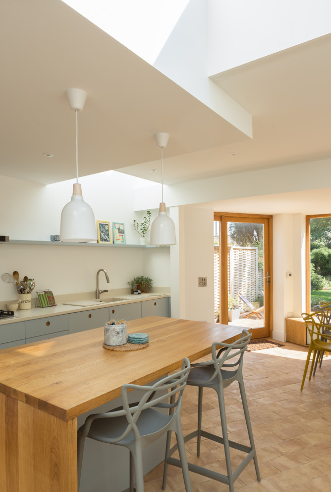 Mid-sized contemporary l-shaped eat-in kitchen in Cambridgeshire with an integrated sink, flat-panel cabinets, blue cabinets, solid surface benchtops, white splashback, stainless steel appliances, terra-cotta floors, with island, pink floor and beige benchtop.