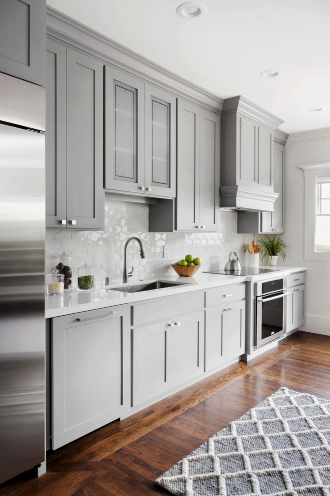 This is an example of a large transitional single-wall kitchen in San Francisco with an undermount sink, shaker cabinets, grey cabinets, solid surface benchtops, white splashback, ceramic splashback, stainless steel appliances and dark hardwood floors.