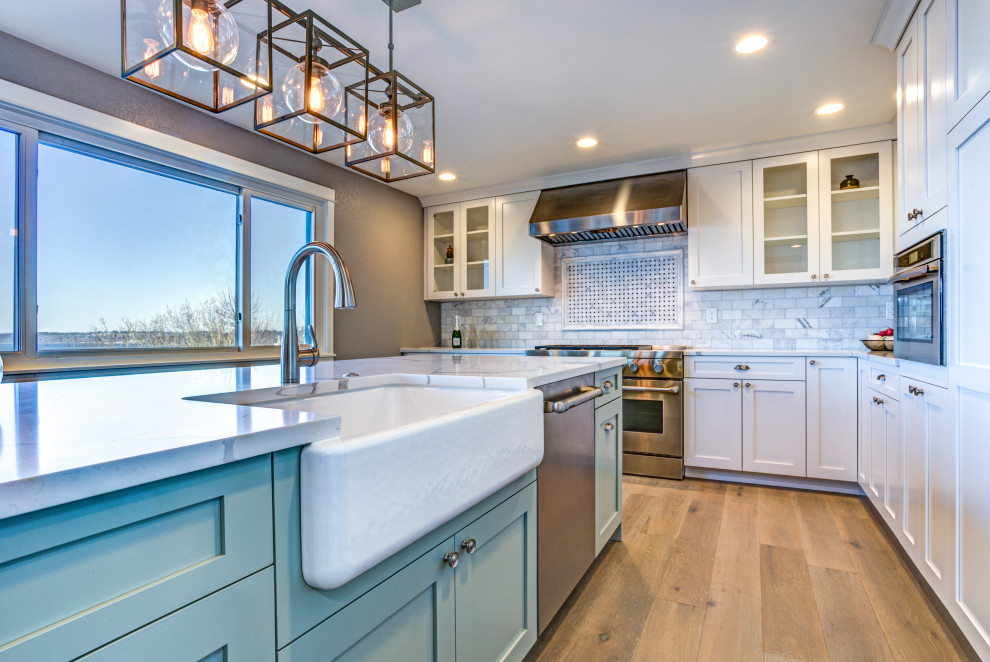 Photo of a mid-sized modern l-shaped eat-in kitchen in San Francisco with a farmhouse sink, shaker cabinets, blue cabinets, quartz benchtops, grey splashback, ceramic splashback, stainless steel appliances, light hardwood floors, with island, brown floor and white benchtop.