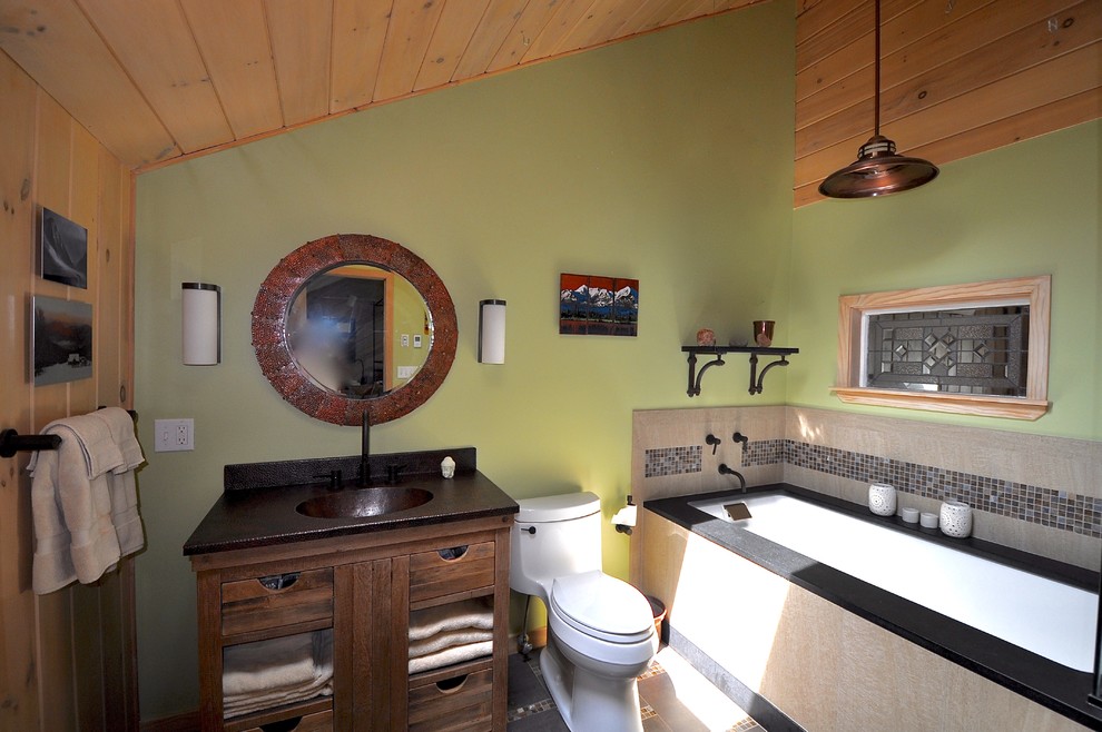 This is an example of a mid-sized arts and crafts master bathroom in Manchester with an integrated sink, furniture-like cabinets, medium wood cabinets, copper benchtops, an undermount tub, a one-piece toilet, brown tile, mosaic tile, green walls and porcelain floors.