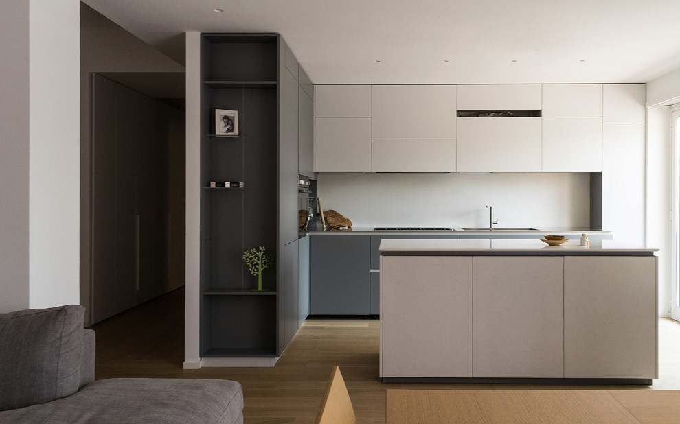 Photo of a mid-sized modern l-shaped eat-in kitchen in Rome with an integrated sink, flat-panel cabinets, grey cabinets, stainless steel benchtops, white splashback, stainless steel appliances, light hardwood floors and with island.