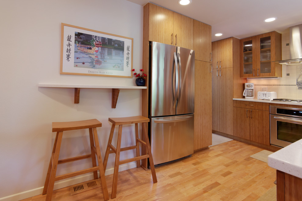 Photo of a mid-sized asian u-shaped eat-in kitchen in Portland with a drop-in sink, flat-panel cabinets, medium wood cabinets, quartz benchtops, white splashback, subway tile splashback, stainless steel appliances, light hardwood floors and no island.