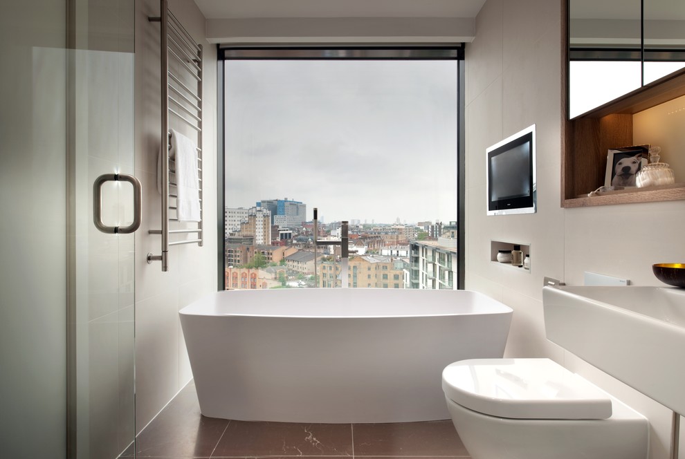 Inspiration for a small contemporary master bathroom in London with a freestanding tub, a wall-mount toilet, beige walls, beige tile and brown floor.