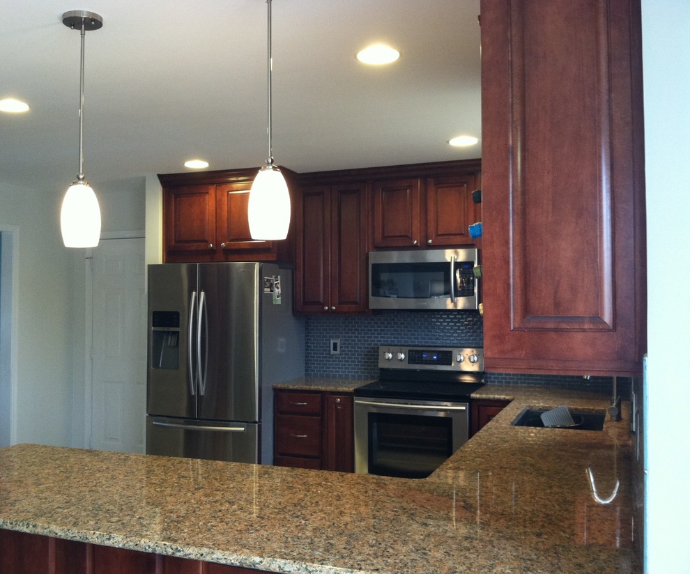 Example of a large transitional u-shaped ceramic tile and beige floor enclosed kitchen design with an undermount sink, raised-panel cabinets, dark wood cabinets, granite countertops, blue backsplash, ceramic backsplash, stainless steel appliances and a peninsula