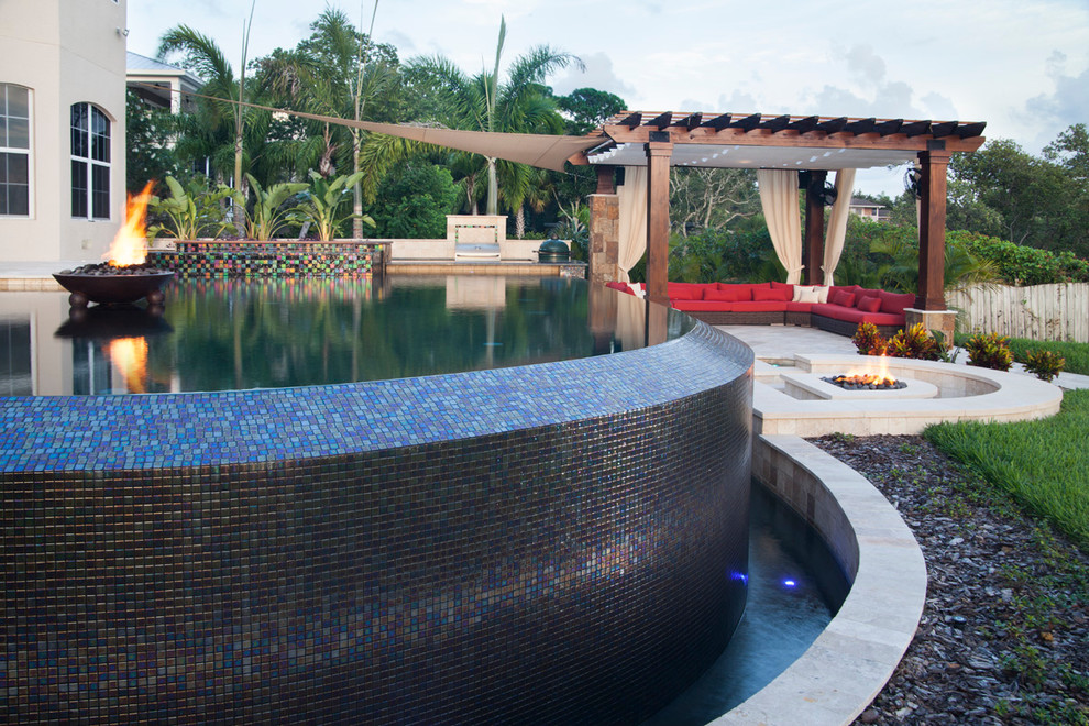This is an example of a large contemporary backyard custom-shaped infinity pool in Tampa with a hot tub and natural stone pavers.