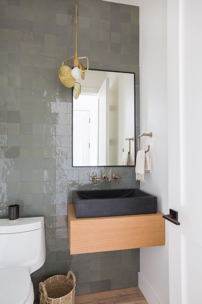 Photo of a beach style powder room in San Diego with flat-panel cabinets, medium wood cabinets, gray tile, white walls, medium hardwood floors, a vessel sink, wood benchtops, brown floor and brown benchtops.