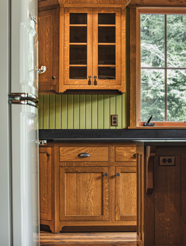 Mountain style medium tone wood floor and exposed beam kitchen photo with an undermount sink, shaker cabinets, granite countertops, black backsplash, granite backsplash, stainless steel appliances, an island and black countertops