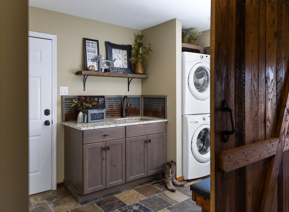 Photo of a mid-sized transitional dedicated laundry room in Other with an undermount sink, shaker cabinets, dark wood cabinets, granite benchtops, beige walls, slate floors, a stacked washer and dryer and multi-coloured floor.