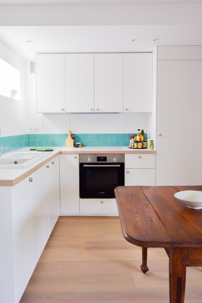 Inspiration for a mid-sized scandinavian l-shaped open plan kitchen in Paris with a single-bowl sink, flat-panel cabinets, white cabinets, laminate benchtops, blue splashback, terra-cotta splashback, stainless steel appliances, light hardwood floors, beige floor and white benchtop.