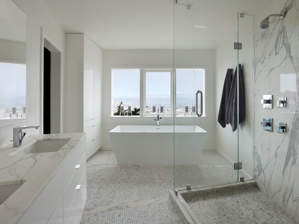 This is an example of a large transitional master bathroom in San Francisco with flat-panel cabinets, white cabinets, a freestanding tub, an open shower, a one-piece toilet, gray tile, white tile, stone slab, white walls, mosaic tile floors, a drop-in sink and marble benchtops.