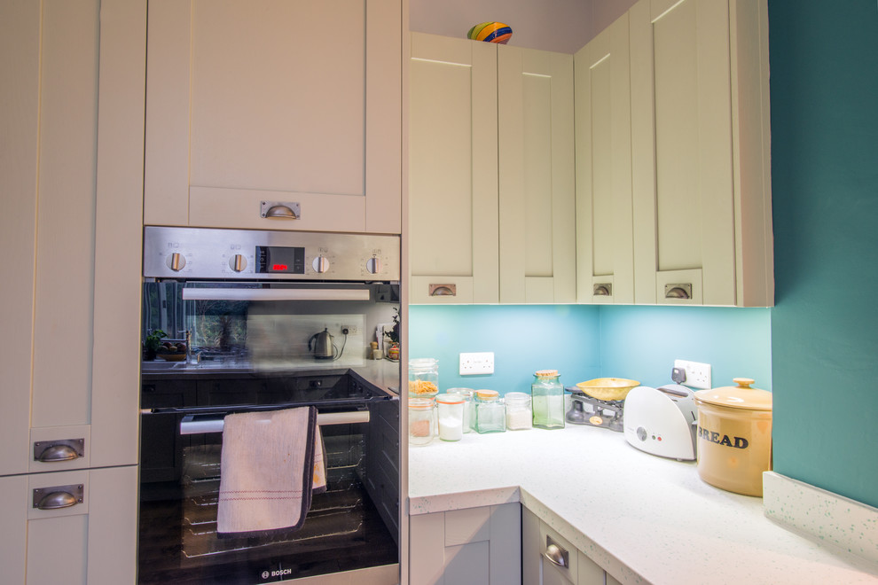 Mid-sized contemporary u-shaped eat-in kitchen in Other with a double-bowl sink, shaker cabinets, green cabinets, solid surface benchtops, white splashback, panelled appliances, light hardwood floors and no island.
