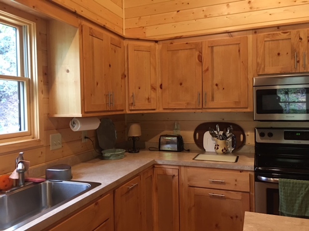 Kitchen - large rustic l-shaped medium tone wood floor and brown floor kitchen idea with a double-bowl sink, shaker cabinets, light wood cabinets, solid surface countertops, brown backsplash, wood backsplash and stainless steel appliances