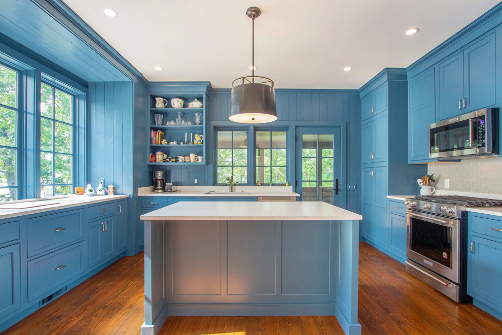 Design ideas for a country u-shaped kitchen pantry in Grand Rapids with an undermount sink, shaker cabinets, blue cabinets, granite benchtops, grey splashback, subway tile splashback, stainless steel appliances, dark hardwood floors, with island, brown floor and white benchtop.