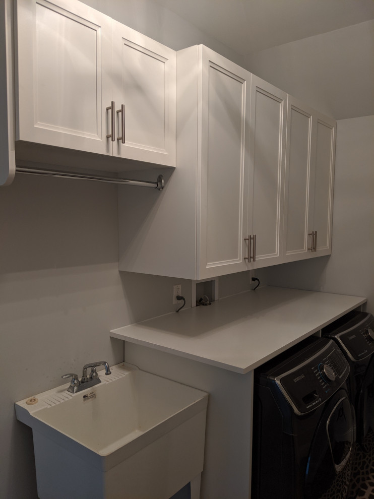 Photo of a small traditional single-wall utility room in New York with an utility sink, raised-panel cabinets, white cabinets, quartz benchtops, grey walls, a side-by-side washer and dryer and white benchtop.