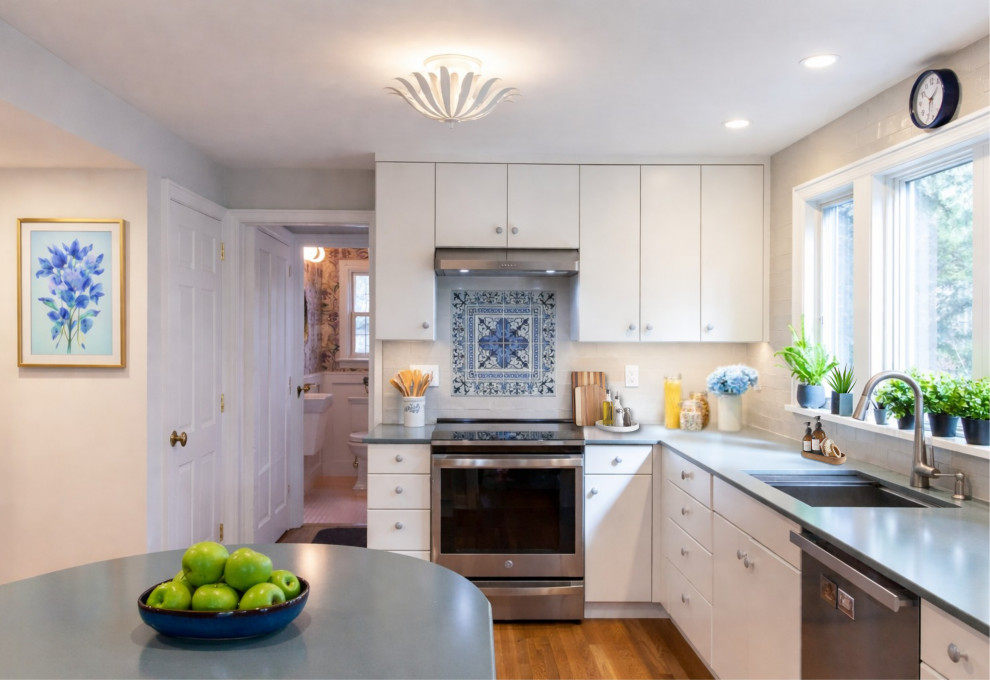 Inspiration for a mid-sized transitional l-shaped medium tone wood floor and brown floor enclosed kitchen remodel in New York with a drop-in sink, flat-panel cabinets, white cabinets, soapstone countertops, white backsplash, ceramic backsplash, stainless steel appliances, an island and blue countertops