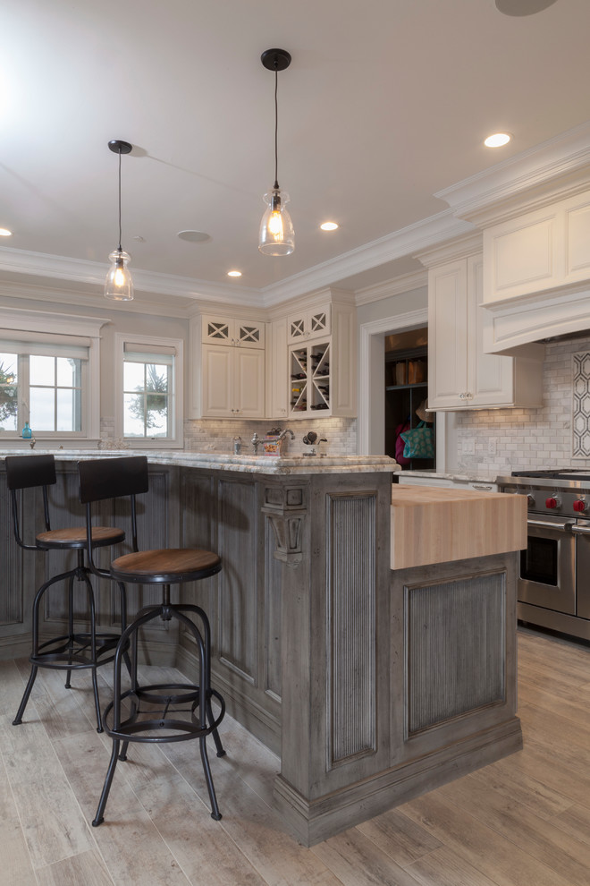 Inspiration for a large traditional u-shaped eat-in kitchen in New York with a farmhouse sink, raised-panel cabinets, white cabinets, granite benchtops, grey splashback, porcelain splashback, stainless steel appliances, ceramic floors and with island.
