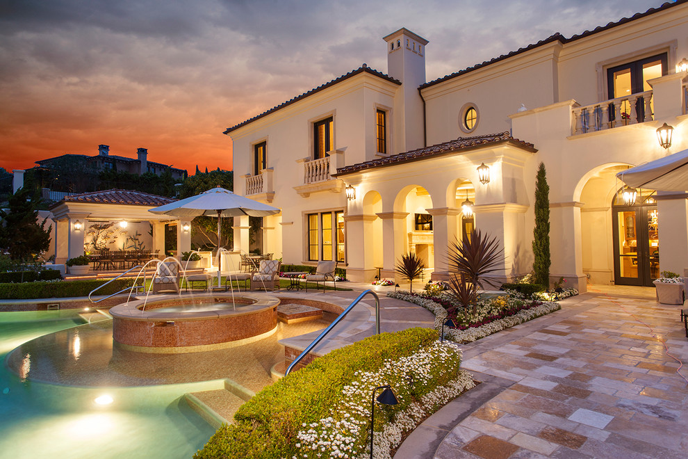 Inspiration for an expansive mediterranean backyard custom-shaped infinity pool in Orange County with a pool house and natural stone pavers.