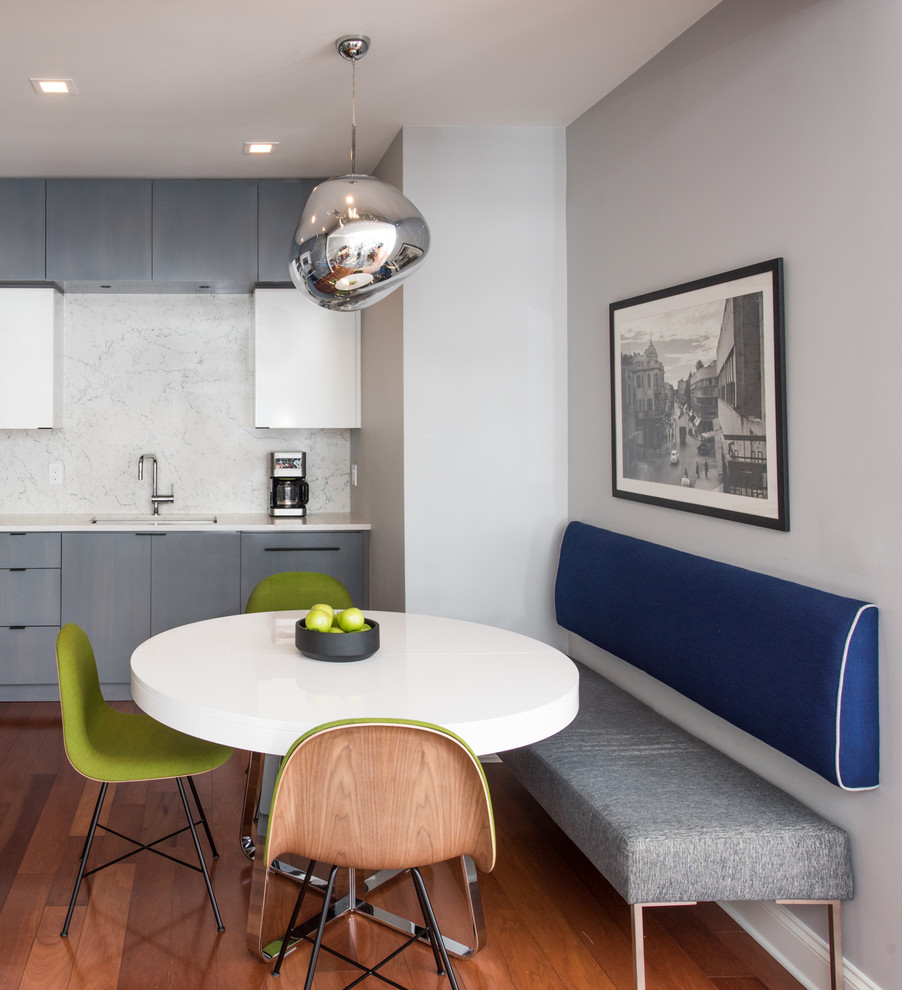 Small contemporary l-shaped eat-in kitchen in New York with an undermount sink, flat-panel cabinets, grey cabinets, quartz benchtops, white splashback, stone slab splashback, panelled appliances, medium hardwood floors, no island, brown floor and white benchtop.
