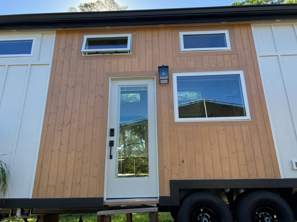 Esempio della micro casa piccola multicolore country a un piano con rivestimento in legno, tetto a capanna, copertura in metallo o lamiera, tetto nero e pannelli e listelle di legno