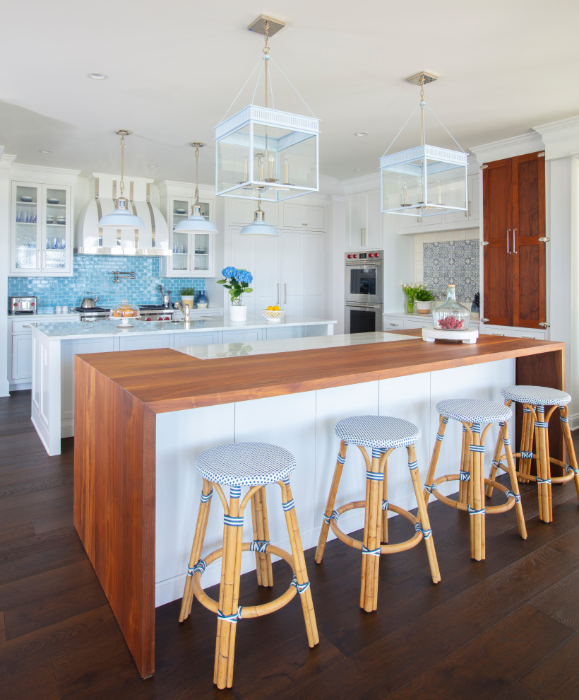 Beach style u-shaped kitchen in Baltimore with a farmhouse sink, shaker cabinets, white cabinets, wood benchtops, blue splashback, subway tile splashback, stainless steel appliances, dark hardwood floors, multiple islands, brown floor and brown benchtop.