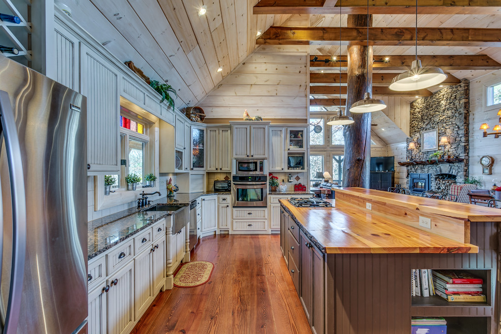 Country l-shaped open plan kitchen in Atlanta with a farmhouse sink, recessed-panel cabinets, beige cabinets, wood benchtops, stainless steel appliances, medium hardwood floors and with island.