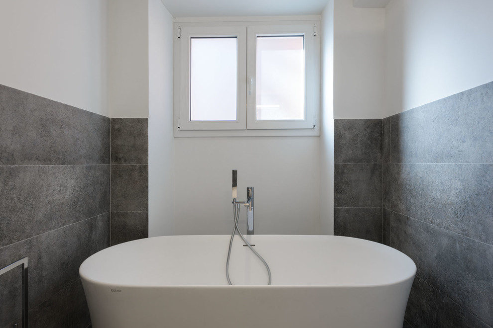 This is an example of a large contemporary master bathroom in Rome with open cabinets, grey cabinets, a freestanding tub, a wall-mount toilet, gray tile, porcelain tile, grey walls, porcelain floors, a vessel sink, limestone benchtops and grey floor.