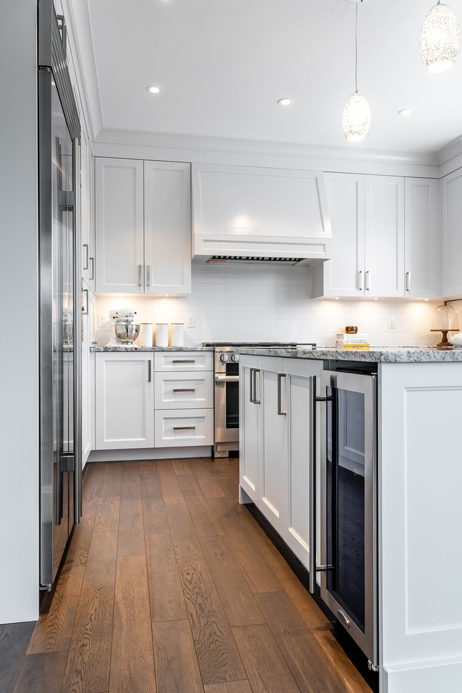 Inspiration for a large transitional u-shaped medium tone wood floor and brown floor eat-in kitchen remodel in Vancouver with an undermount sink, recessed-panel cabinets, white cabinets, granite countertops, white backsplash, subway tile backsplash, stainless steel appliances, an island and multicolored countertops
