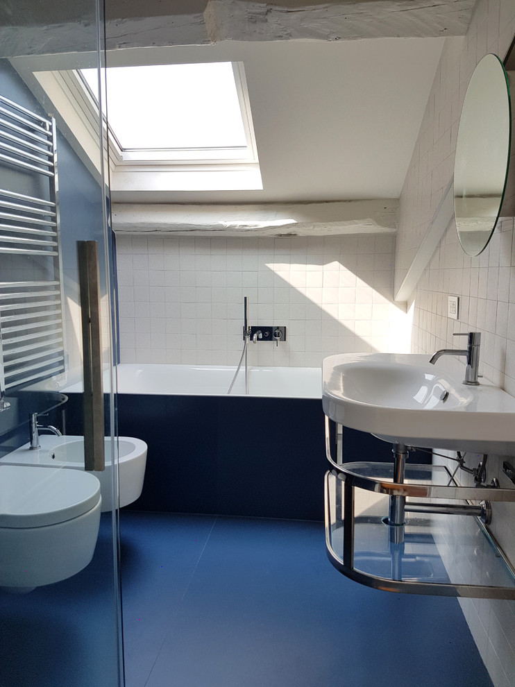 This is an example of a small contemporary 3/4 bathroom in Milan with a drop-in tub, a curbless shower, a two-piece toilet, white tile, ceramic tile, white walls, porcelain floors, a wall-mount sink, blue floor, a hinged shower door, a single vanity and exposed beam.