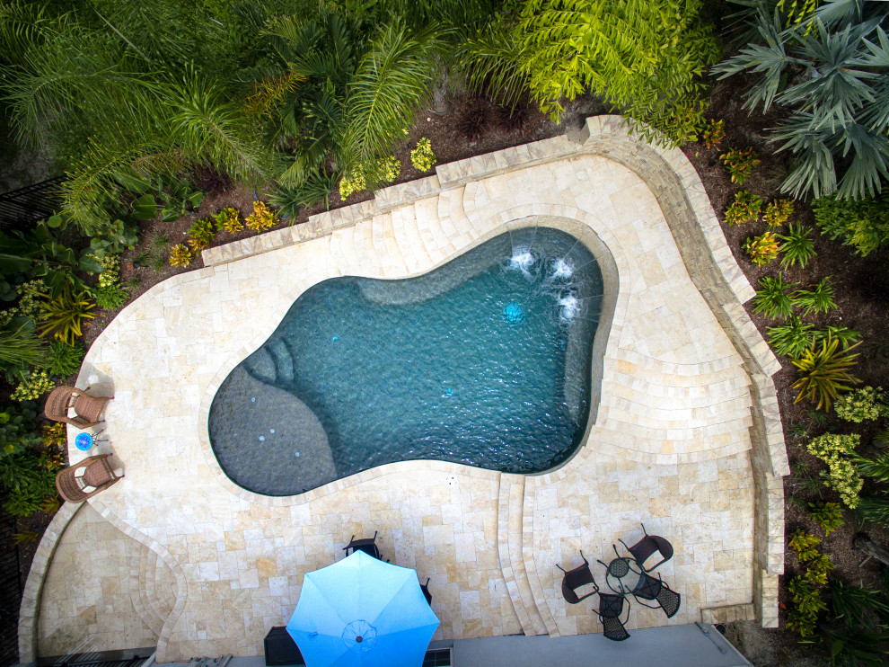 Photo of a tropical backyard custom-shaped pool in Orlando with with a pool and natural stone pavers.
