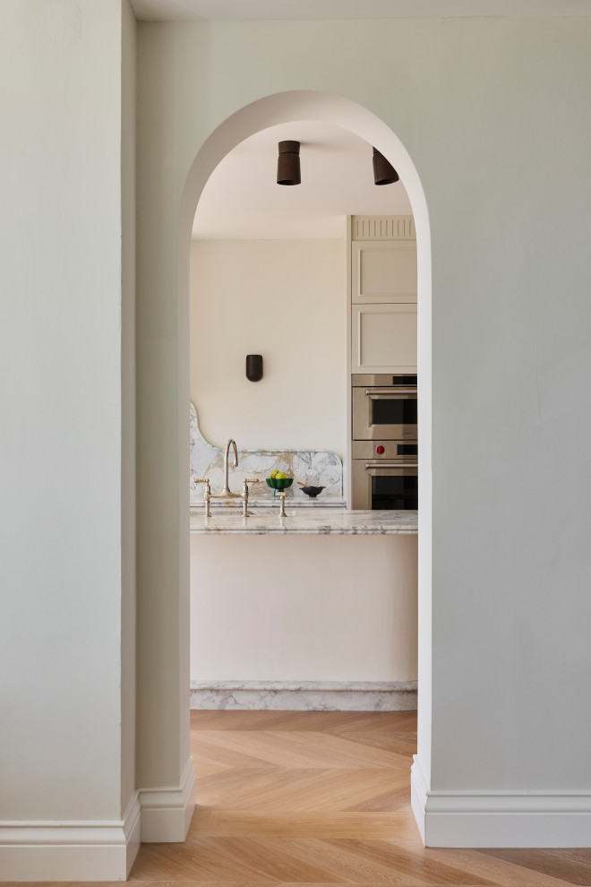 Expansive mediterranean l-shaped kitchen pantry in Sydney with an undermount sink, beaded inset cabinets, beige cabinets, marble benchtops, grey splashback, marble splashback, stainless steel appliances, light hardwood floors, with island, brown floor and grey benchtop.