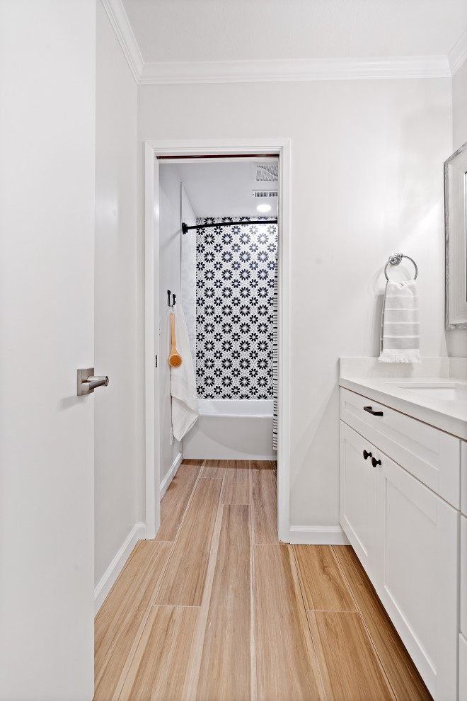 This is an example of a mid-sized beach style kids bathroom in San Francisco with recessed-panel cabinets, white cabinets, an alcove tub, an alcove shower, a two-piece toilet, black and white tile, ceramic tile, white walls, vinyl floors, an undermount sink, engineered quartz benchtops, brown floor, a shower curtain, white benchtops, a built-in vanity and a single vanity.