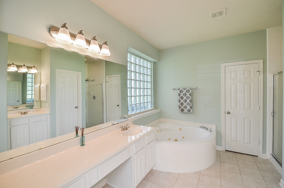 This is an example of a large traditional master bathroom in Houston with raised-panel cabinets, white cabinets, a corner tub, an alcove shower, a two-piece toilet, white tile, cement tile, green walls, ceramic floors, an integrated sink, solid surface benchtops, beige floor, a hinged shower door and white benchtops.