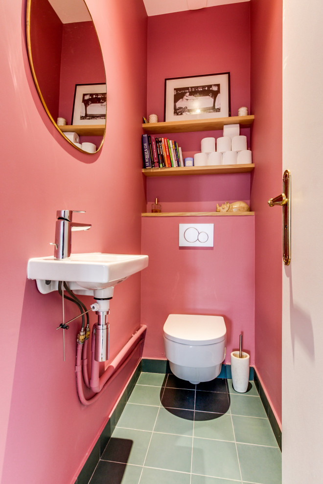 This is an example of a mid-sized contemporary powder room in Paris with a wall-mount toilet, pink walls, ceramic floors, a wall-mount sink and green floor.