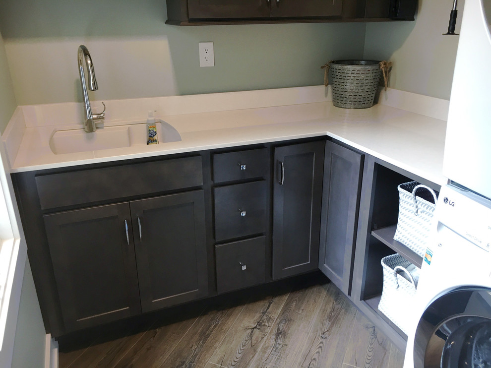 This is an example of a large modern l-shaped utility room in Other with an undermount sink, shaker cabinets, grey cabinets, quartz benchtops, grey walls, medium hardwood floors, a stacked washer and dryer and grey floor.