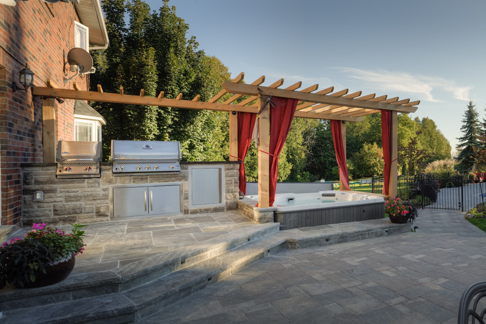 Idée de décoration pour une grande terrasse arrière tradition avec une cuisine d'été, des pavés en pierre naturelle et une pergola.