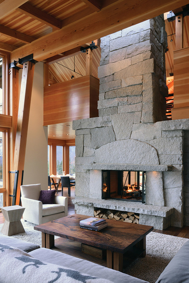 This is an example of a mid-sized country formal open concept living room in Other with a two-sided fireplace, a stone fireplace surround, multi-coloured walls, medium hardwood floors and no tv.