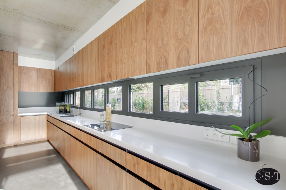 Photo of a large contemporary l-shaped eat-in kitchen in Paris with an undermount sink, beaded inset cabinets, medium wood cabinets, solid surface benchtops, white splashback, panelled appliances, concrete floors, with island, grey floor and white benchtop.