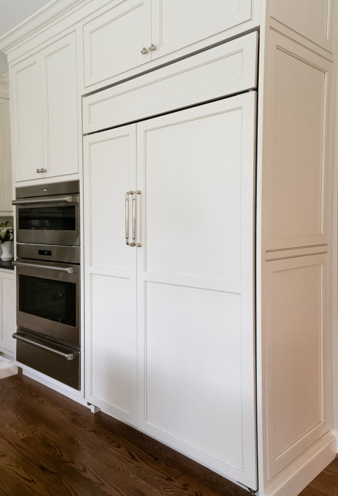 Large traditional u-shaped open plan kitchen in Philadelphia with a farmhouse sink, beaded inset cabinets, white cabinets, granite benchtops, white splashback, subway tile splashback, panelled appliances, medium hardwood floors, with island, brown floor and black benchtop.