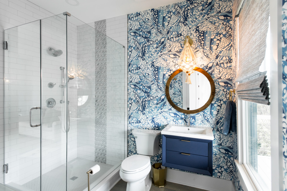 Mid-sized beach style 3/4 bathroom in Charleston with blue cabinets, a corner shower, a two-piece toilet, white tile, subway tile, multi-coloured walls, medium hardwood floors, an integrated sink, a hinged shower door, white benchtops, a single vanity, a floating vanity and wallpaper.