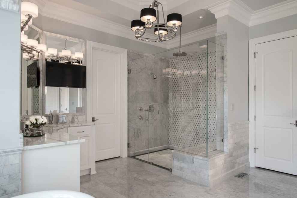 This is an example of a large traditional master bathroom in St Louis with raised-panel cabinets, white cabinets, a one-piece toilet, gray tile, white tile, stone slab, grey walls, porcelain floors, a drop-in sink, a claw-foot tub, a curbless shower and marble benchtops.