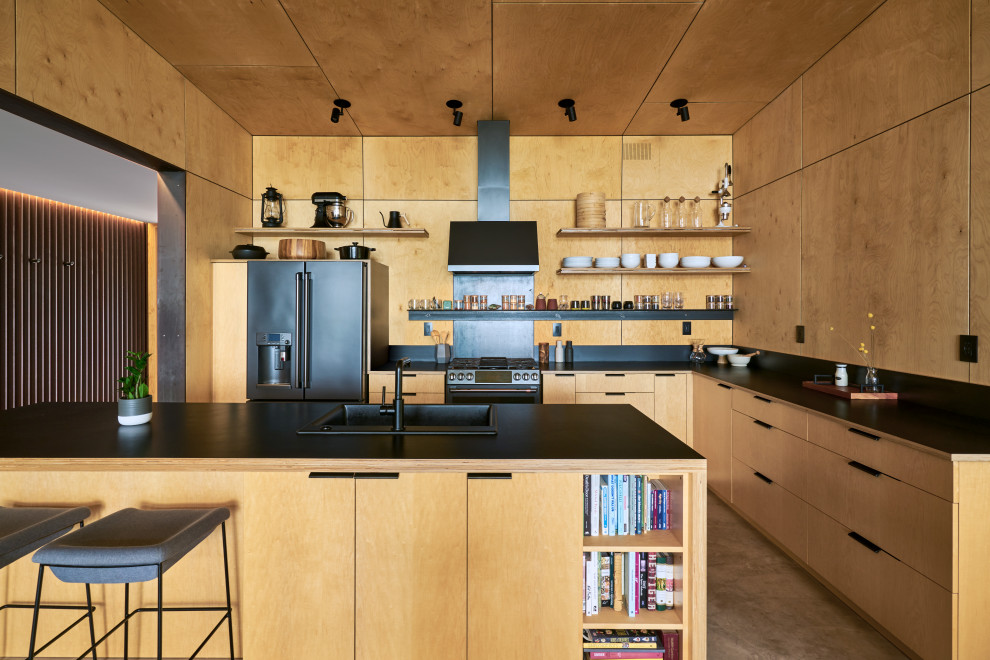 This is an example of a country open plan kitchen in Seattle with light wood cabinets, black appliances, concrete floors, with island and wood.